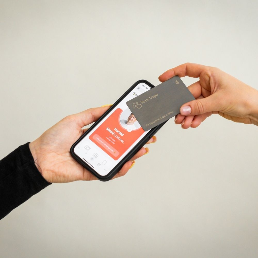 Brushed Metal Grey NFC Business Card being tapped by a mobile phone displaying an open digital business card