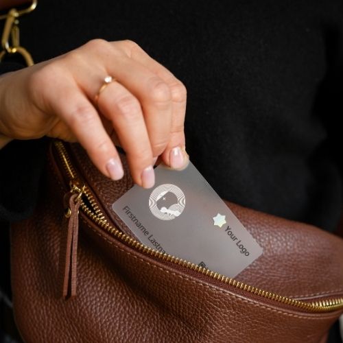 Transparente NFC Visitenkarte wird auf brauner Tasche gezogen.